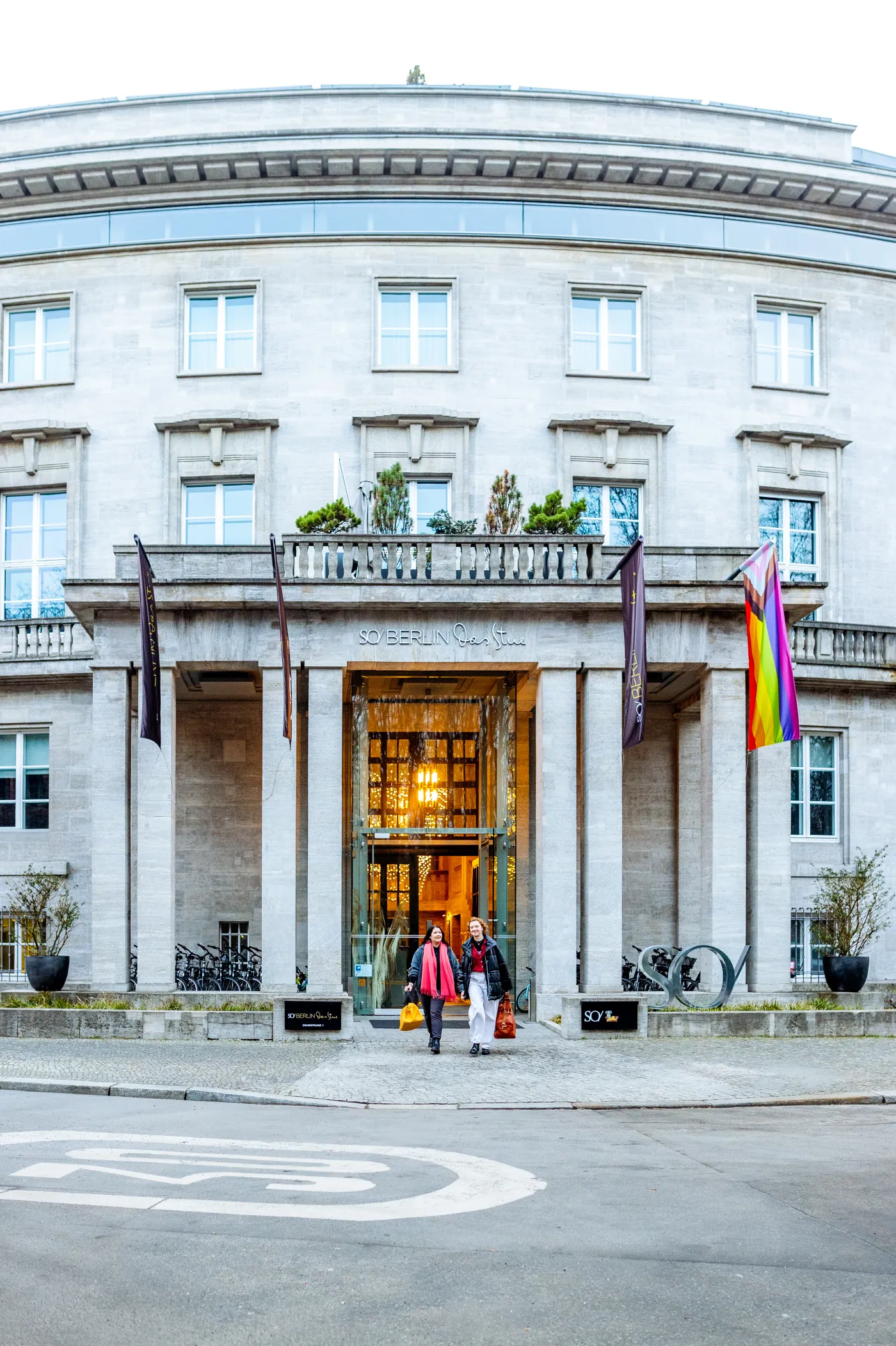 Zwei Frauen verlassen lächelnd den Säuleneingang eines herrschaftlichen Hotelgebäudes