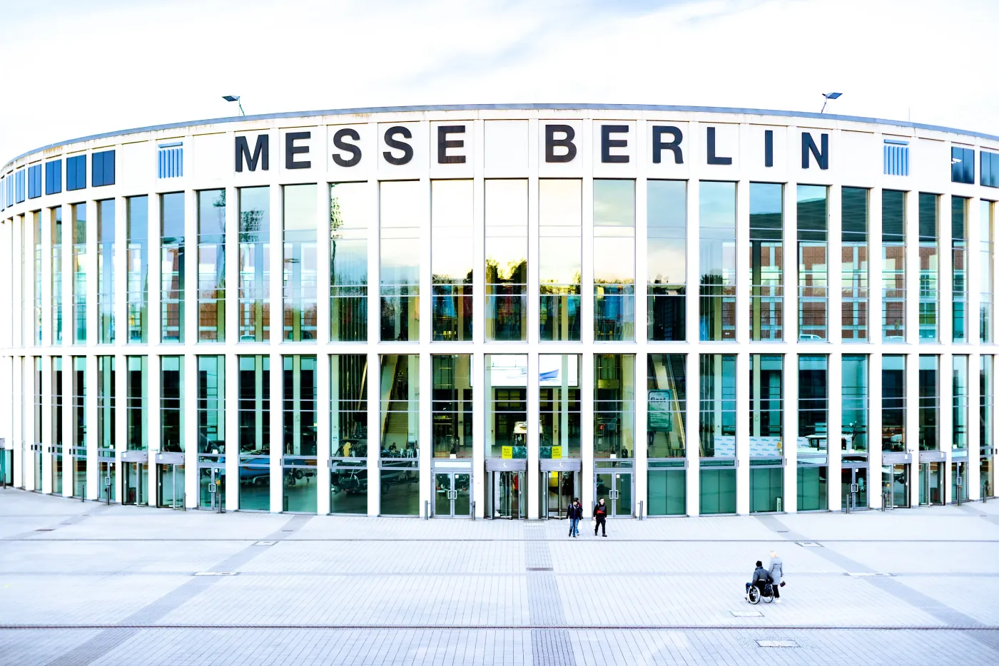 Glasfassade der Messe Berlin mit großer Gebäudebeschriftung und Besuchern auf dem Vorplatz
