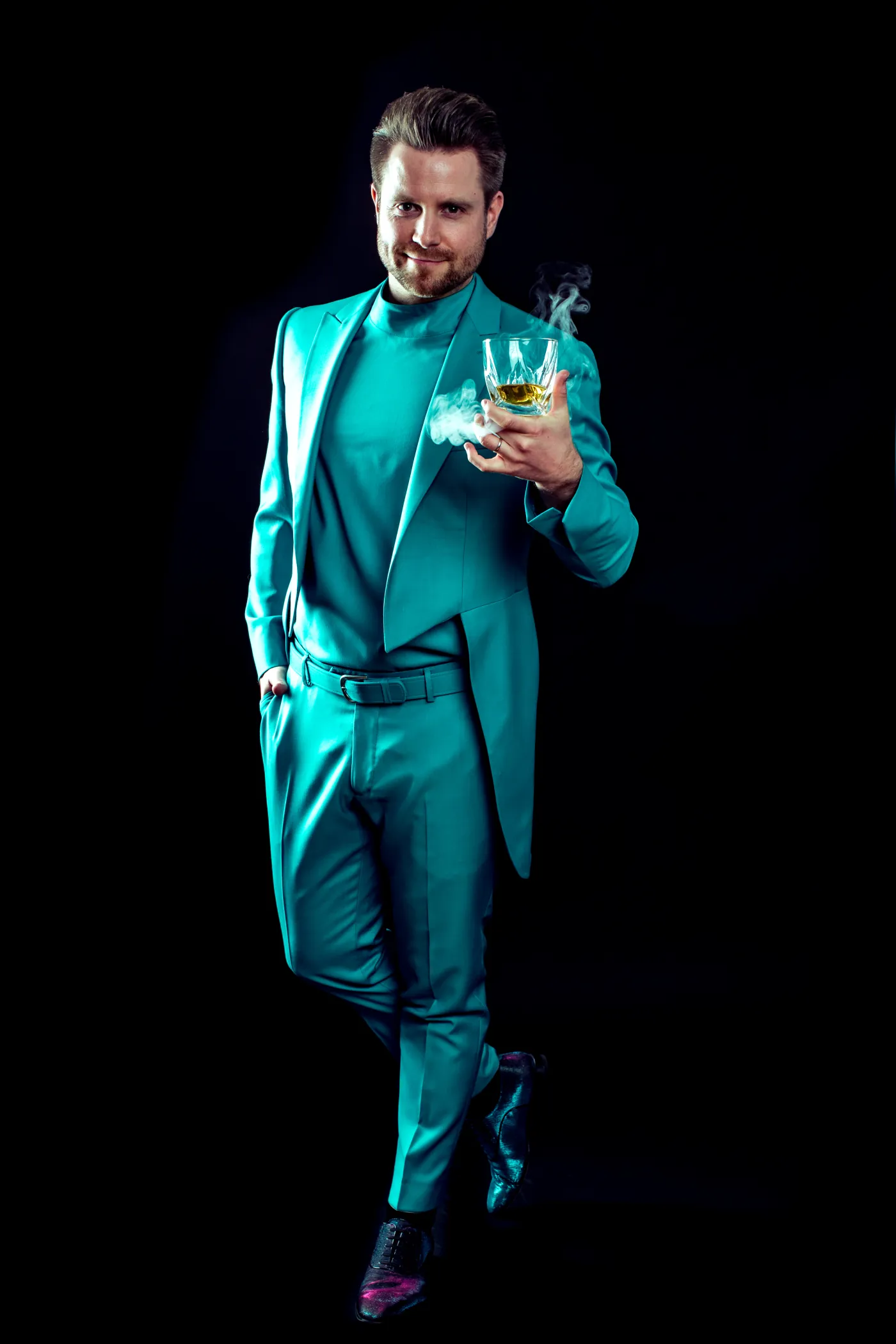 Cody Stone in türkisfarbenem Anzug mit Whiskeyglas vor schwarzem Hintergrund