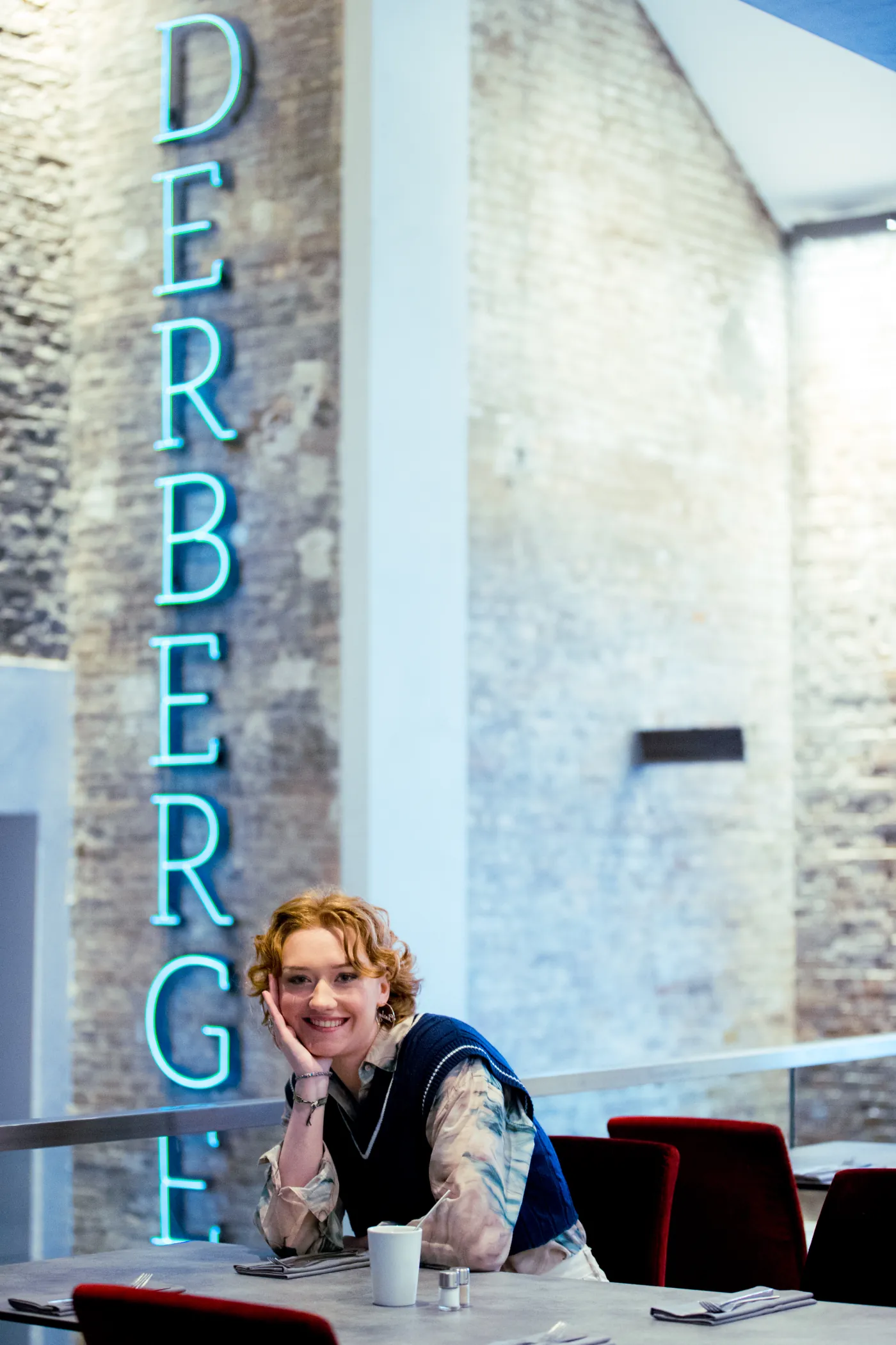 Eine Frau lächelt an einem Tisch vor einer Leuchtschrift-Wand